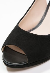 Chaussure pour femme en daim noir à bout ouvert avec doublure intérieure beige et semelle noire, présentée en gros plan sur un fond blanc.