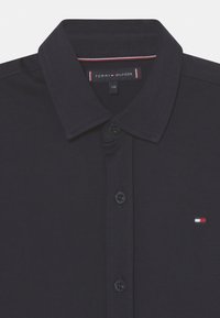Polo blu navy con colletto, pattina con bottoni e un piccolo logo ricamato in rosso, bianco e blu sul petto. Materiale in cotone.