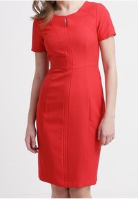 Rode nauwsluitende jurk met korte mouwen, voorzien van een ronde halslijn en een keyholedetail. Gemaakt van glad, gestructureerd materiaal met verticale naden.