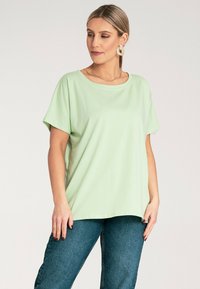 Jasnozielona koszulka z krótkim rękawem, okrągłym dekoltem, luźnym kroju i miękkiego materiału, w połączeniu z niebieskimi dżinsami.