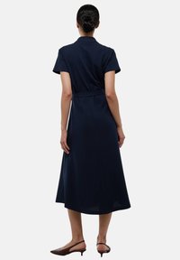 Robe bleu marine à manches courtes, taille cintrée et jupe fluide. Tissu lisse, longueur mi-mollet et col. Accentuée par une ceinture.