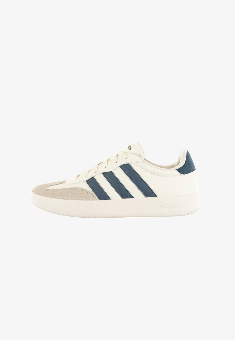 White sneaker with navy blue stripes, suede toe cap, and textured accents. Features a rubber sole and flat laces for closure.