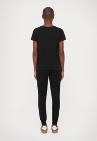 T-shirt de algodão preto combinado com calças de treino pretas e ténis castanhos e verdes. Design simples, corte reto, sem padrões visíveis.