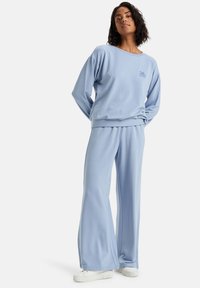 Světlomodrý svetr a kalhoty širokého střihu, vyrobené z měkké tkaniny. Má pohodlný střih s vroubkovanými manžetami a malým logem na hrudi.