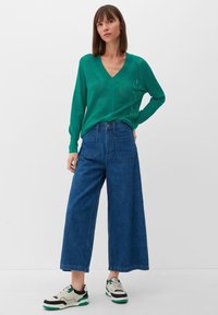 Groene gebreide V-hals pullover met een ademend, textuurpatroon, gecombineerd met high-waisted, wijdvallende blauwe denimbroeken en sneakers.