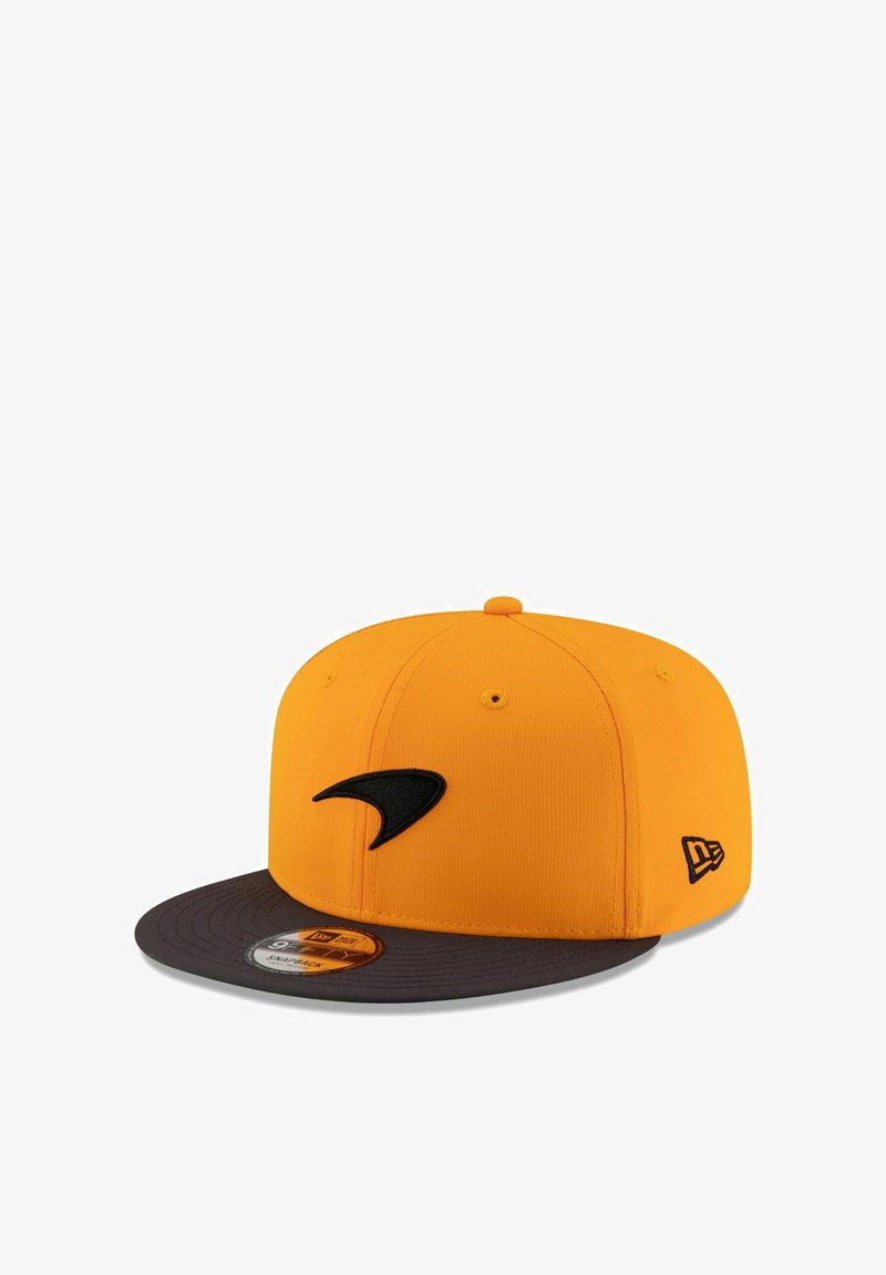 Casquette jaune avec un logo noir à l'avant, une visière gris foncé et un tissu texturé. Comprend un autocollant de taille circulaire sur la visière.