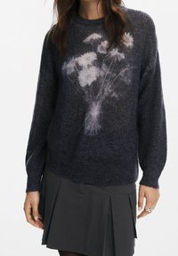 Pull bleu marine avec une texture douce et un imprimé floral blanc délavé à l'avant. Manches longues et encolure ronde. À associer avec une jupe plissée foncée.