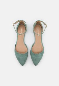 Bailarinas verdes de ante con punta afilada, bordes en forma de olas y tiras para el tobillo. El interior presenta una plantilla en tono beige claro. Acentos mínimos de herrajes.