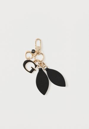 Χρυσό μπρελόκ με μαύρο γοητευτικό γράμμα G, μικρό στρογγυλό γοητευτικό και δύο μαύρα δερμάτινα κρεμαστά φύλλα σε λευκό φόντο.