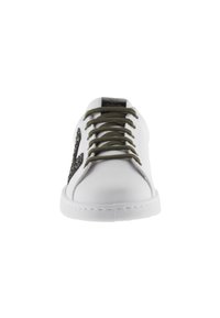 Sneaker bianca in pelle con lacci verdi, caratterizzata da un dettaglio laterale glitterato nero e una suola in gomma testurizzata. Design minimalista.