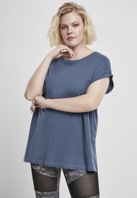 Plava pamučna majica s kratkim rukavima i okruglim izrezom. Uparena s uzorkovanim sivoj tajicama koje imaju mrežaste akcentne detalje na bedro. 