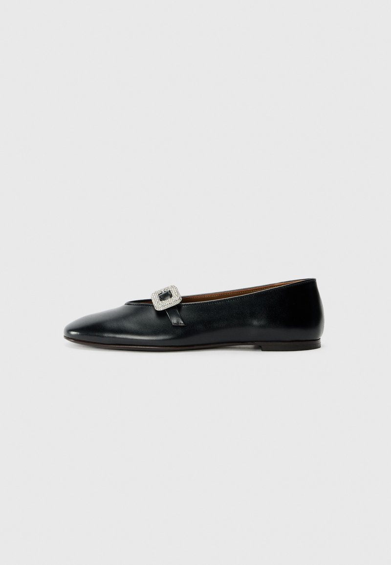 Chaussure plate en cuir noir avec un bout pointu, ornée d'une boucle carrée. Texture lisse avec un petit talon.