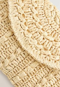 Sac à main en paille beige tissée avec un motif tressé et une fermeture à rabat arrondie, mettant en valeur son design texturé et fait main.