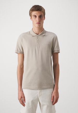 Beige polo krekls, kas izgatavots no kokvilnas, ar trīs pogu kaklu, īsām piedurknēm un smalku izšūtu logo kreisajā krūtī.