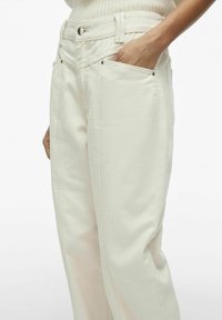 Pantalones de mezclilla color crema con corte recto, que cuentan con bolsillos laterales y detalles de herrajes negros. Diseñados con costuras visibles.
