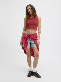 Piros bordázott crop top, világoskék farmer rövidnadrág cakkos szegéllyel, piros kockás ing megkötve a derékon, fehér zoknik, fekete fűzős cipők.