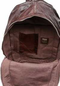 Zaino in pelle marrone aperto che mostra un interno in tessuto con una piccola tasca in pelle e un'etichetta di metallo del marchio.