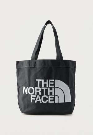 Melna pleca soma ar divām rokturi, uz priekšpuses liels balts "The North Face" logotips un dizains uz vienkrāsaina fona.