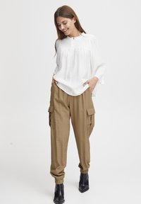 Vit blus med veckad smockdetalj, kompletterad med lösa khaki cargo-byxor med sidofickor och svarta ankelstövlar.