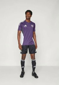 Lilla fotballdrakt med vita detaljer, matchande svarta shorts och svarta strumpor. Har Adidas-logotyper och ränder.