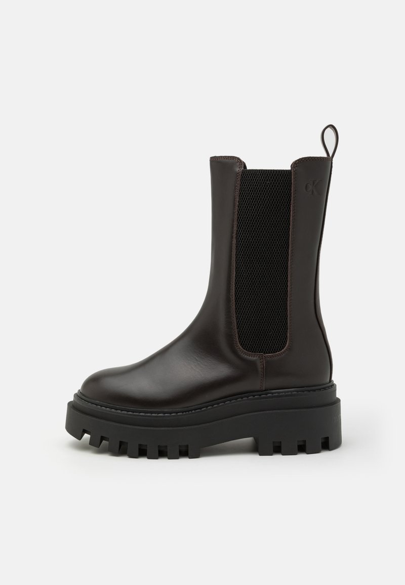 Brown leather ankle boots with a textured elastic panel, thick black rubber sole, and pull tab. Sleek design with minimal stitching.