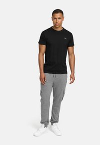 T-shirt en coton noir à manches courtes et encolure ronde, associé à un jogging cargo gris avec poches latérales et poignets élastiques. Baskets blanches.