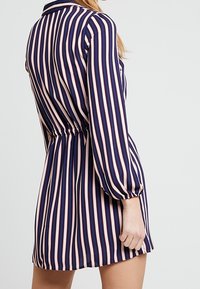 Námořnické a růžové pruhované šaty s límečkem, dlouhými nafouklými rukávy a nařaseným pasem. Hladká látka s vodorovnými a svislými vzory.