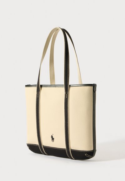 Saco de tote em lona em bege com detalhes pretos, apresentando alças duplas, costura contrastante e um pequeno detalhe com logotipo na base.