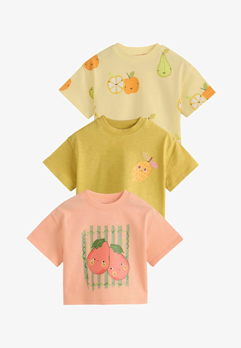 Trois t-shirts colorés pour enfants avec des motifs de fruits souriants : jaune avec des poires et des oranges, olive avec un ananas, et pêche avec deux pêches.