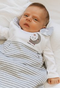 Baumwoll-Babykleidung mit einem weißen Oberteil, das ein Mond- und Sternenmotiv zeigt, und einem gestreiften grauen Unterteil. Der Stoff ist weich und hat auffällige, strukturierte Akzente.