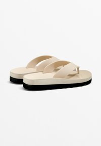 Ljusbeige flip-flops med tre breda remmar och en strukturerad sula, med en svart gummiyttersula för grepp och hållbarhet.