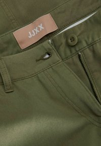 Pantalones de algodón verde oliva con cierre de cremallera y botón, con una etiqueta rosa que dice "JJXX" en el interior de la cinturilla.