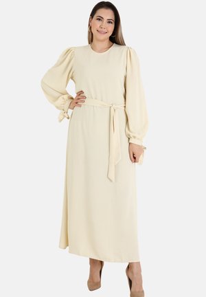 Long, cream-colored dress with puff sleeves and a belted waist. Made from a soft fabric, featuring tie accents at the sleeve hems.