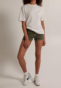 Camiseta de algodón blanca con cuello redondo y mangas cortas, combinada con pantalones cortos de color verde oliva. Zapatillas blancas y negras completan el conjunto.
