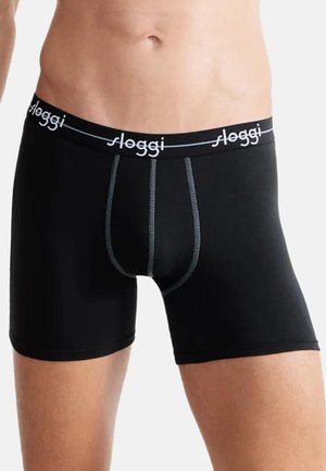 Männlicher Oberkörper trägt schwarze Boxershorts mit kontrastierender grauer Naht und schwarzem Bund, der mit weißen Buchstaben "Sloggi" gebrandmarkt ist.