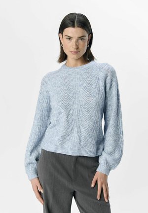 Un pull en tricot bleu clair avec un motif texturé, des poignets et un ourlet côtelés, porté avec un pantalon gris. Le design présente un col rond.