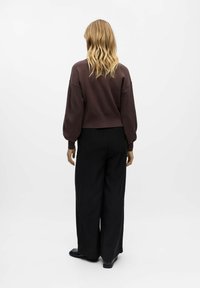 Tamsiai rudas trumpas megztinis su ilgomis, pūkuotomis rankovėmis, derinamas su juodomis plačiomis kelnėmis. Lygi tekstūra, minimalistinis dizainas ir jokios matomos tekstūros.