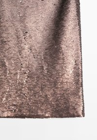 Tessuto di paillettes in oro rosa con paillettes arrotondate e sovrapposte che creano una superficie testurizzata, riflettendo la luce. I bordi sono lisci e rifiniti.