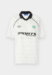 Balta sportinė marškinėliai su juodu apykakle, trumpomis rankovėmis ir lengvų žvaigždžių raštu. Su logotipu "SPORTŲ IŠŠŪKIS" ir numeriu "10" žalia spalva.