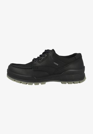 Black leather shoe with a rounded shape, featuring a lace-up design, textured side accents, and a treaded gray rubber outsole.