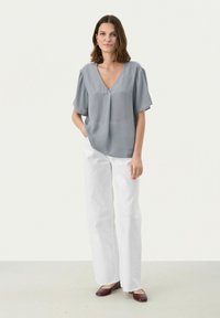 Harmaa, lyhythihainen pusero V-neck-muotoilulla, yhdistettynä valkoisiin leveälahkeisiin housuihin ja marjapunaisiin flats-kenkiin. Sileä rakenne, rento istuvuus.