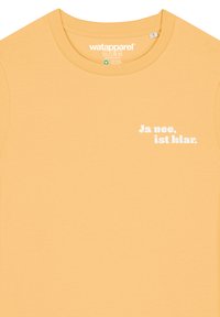 Geel katoenen T-shirt met een ronde hals en korte mouwen. Op de voorkant staat in witte letters "Ja nee, ist klar."