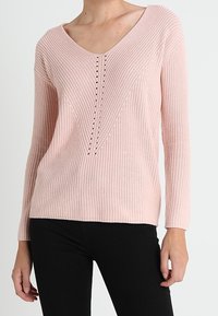 Pull en maille côtelée rose clair avec des manches longues, un col en V et un motif vertical central de petits trous décoratifs.