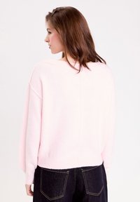 Pull oversized rose clair avec un design à épaule tombante, des poignets et un ourlet côtelés, et une couture au centre du dos. Assorti à un jean en denim foncé.