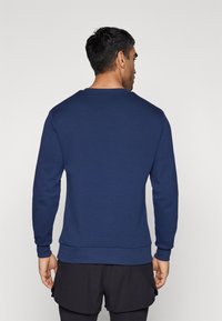 Granatowa bluza wykonana z miękkiego materiału, z okrągłym dekoltem, ściągaczami przy rękawach i w pasie. Gładki wzór, brak widocznych logo lub wzorów.