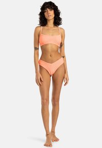 Bikini komplet v breskevasti barvi, ki vključuje pravokotno kratko majico z tankimi naramnicami in hlačkami z visokim pasom. Gladka tekstura, minimalen dizajn in brez vzorcev.