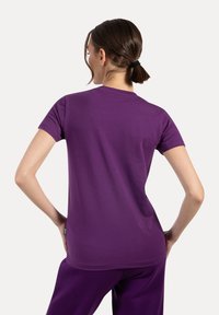 Camiseta corta de manga en color púrpura, hecha de una tela suave, con un cuello redondo, que presenta una textura lisa y un corte recto en el dobladillo.