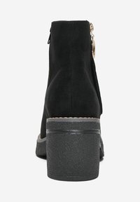 Black suede ankle boot with a textured mid-heel, back zipper, and metal accent. Features a slightly rounded toe and ribbed sole.