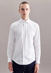 Wit overhemd van gladde stof, voorzien van een puntkraag, lange mouwen en een gebogen zoom met knoopsluiting aan de voorkant.