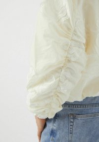 Crème-kleurige blouse met textuur, geborduurde puffmouwen met een geplooid ontwerp. Gedragen met blauwe denim.
